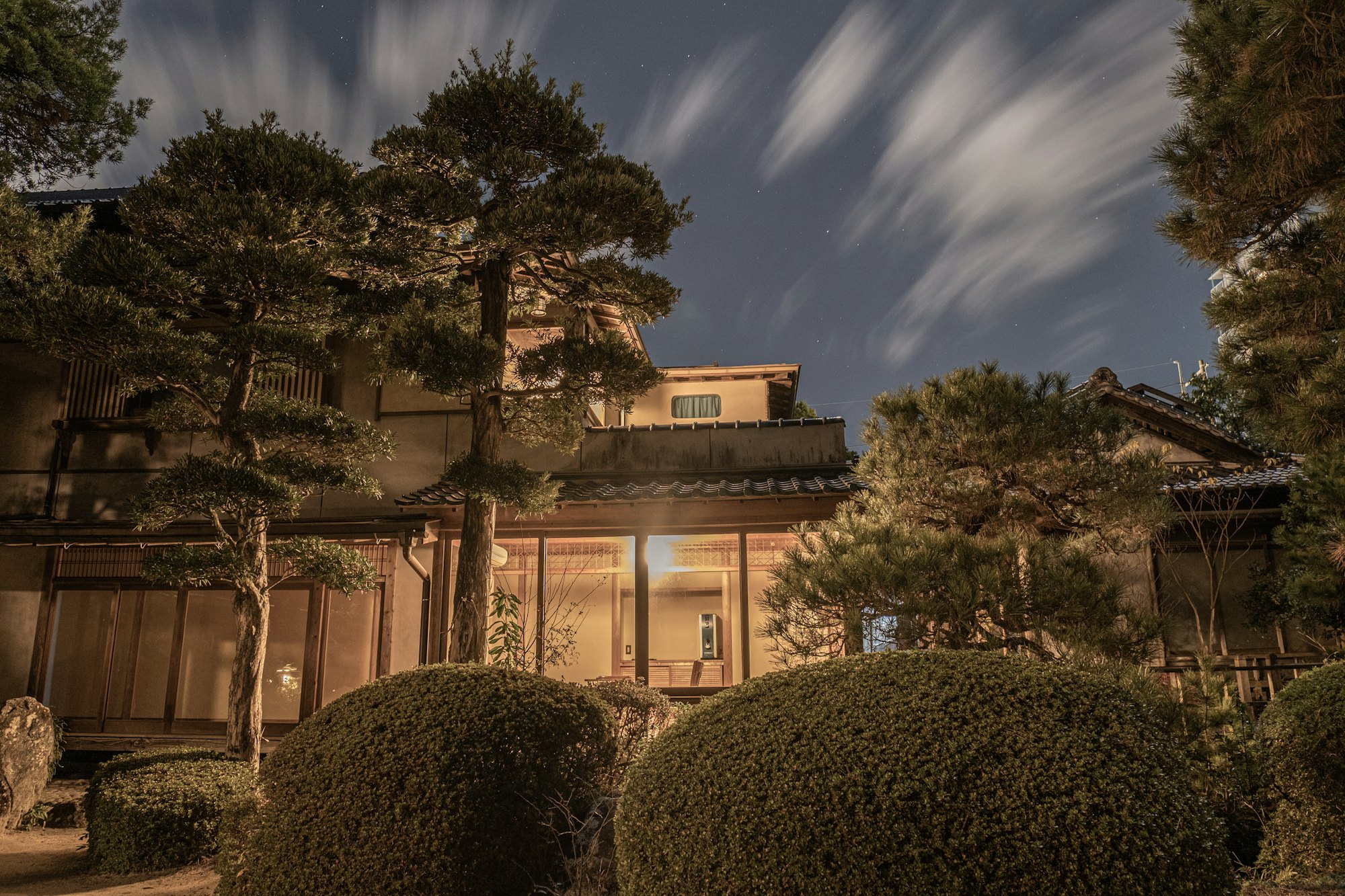 夜空の下、松の庭越しに明かりの灯る旅館